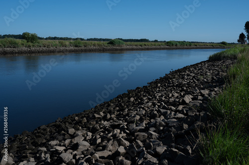 A quiet river with stony banks, framed by green bank areas, dike landscape on the Hunte in summer in 27798 Hude, Germany
