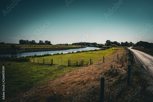 A river meanders through green meadows, accompanied by a narrow path, dike landscape on the Hunte in summer in 27798 Hude, Germany