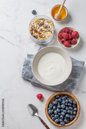 Healthy yogurt breakfast with berries, muesli and honey on marble background