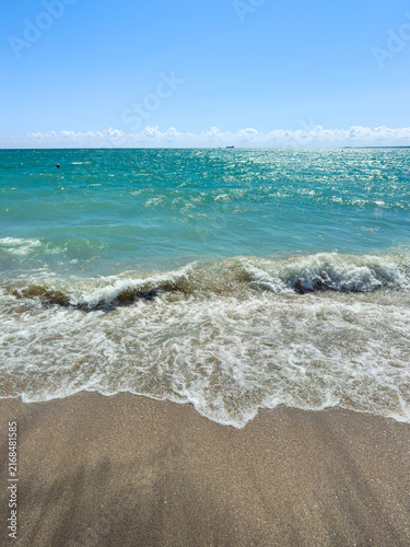 Konstfotografi Waves rolling onto the sandy beach with clear blue water and cloudless sky at mi
