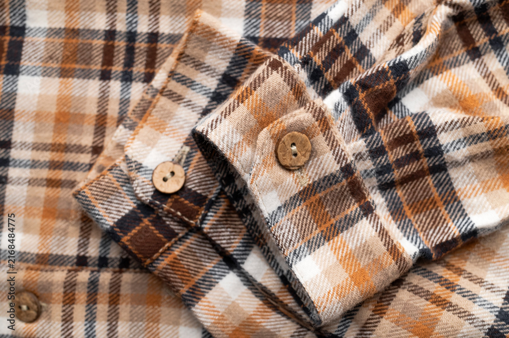 Naklejka premium Close-up of details of plaid flannel fall shirt. Buttons, collar, sleeves, cotton plaid fabric in brown, red, beige tones. Fashionable, stylish clothing concept, texture of cozy fabric.