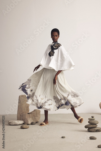 Fashion model in white cape top and floral skirt with stone props