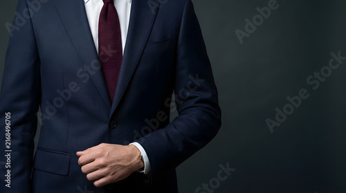 Professional businessman in a dark navy suit and tie, corporate portrait on grey background.