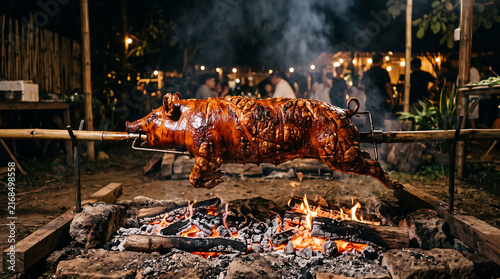 whole pig roasting on spit over open fire charcoal pit at outdoor night party traditional lechon barbecue concept