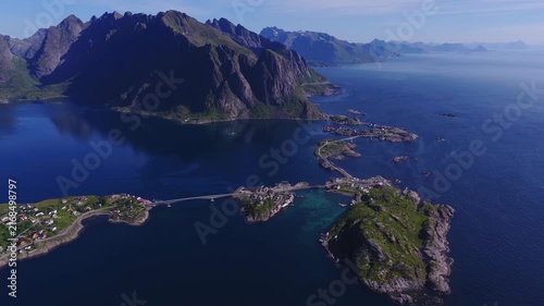 Aerial view shows the bridges connecting small islands and fishing villages with steep mountain peaks in Lofoten, Norway on a clear sunny day.