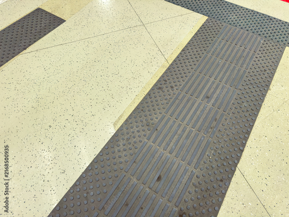 Fototapeta premium Close view of floor textures in a public space showing tiles and matting with tactile indicators