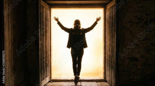 Silhouette of woman walking through open wooden door towards bright golden sunlight, symbolizing new beginnings and success, freedom and liberation, overcoming obstacles