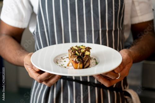 Chef Showcasing a Beautifully Plated Gourmet Dish at a Bustling Restaurant Kitchen