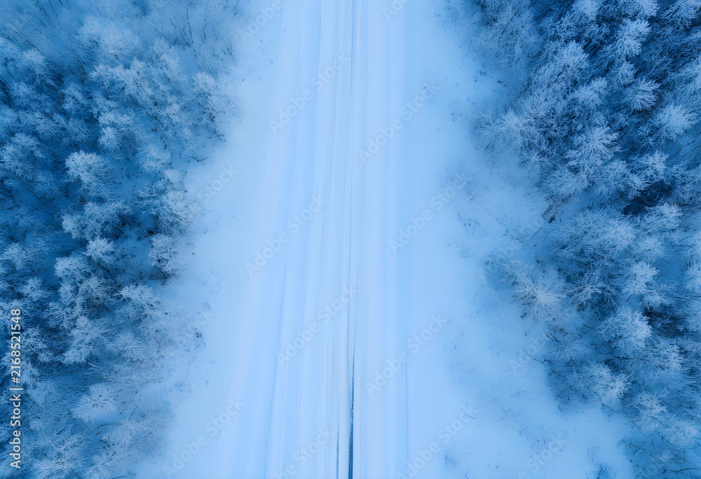 Fototapeta premium Winter road through snow-covered forest, aerial view of cold season landscape and travel, nature background