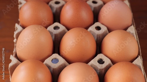 Close-up rotating shot of fresh brown chicken eggs arranged in a row against a dark textured background, food ingredient and farm produce concept.	