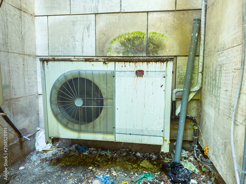 Foto Old air conditioning unit next to a dirty wall covered with stains and trash in