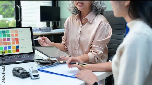 Car dealer agent shows color palette swatches and explains loan agreement contract to senior female buyer