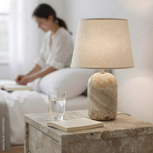 Still-life of a travertine stone lamp and a glass of water on a stone nightstand.