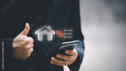 Businessman using telephone and laptop with house interest rate icon. Concept of real estate tax, mortgage loan calculation, financial planning, and home property investment.
