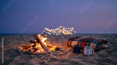 Driftwood bonfire on beach at dusk, warm ocean bokeh 