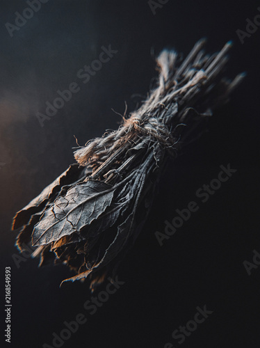 Dried herb bundle tied with twine hanging against dark moody background, rustic botanical still life