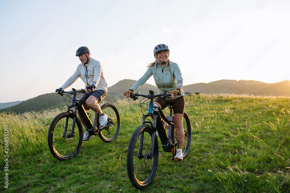 Fototapeta premium Happy mature couple riding e-bikes through scenic countryside.