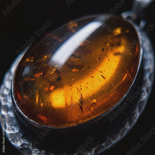 Amber gemstone pendant with inclusions in silver setting, close-up macro jewelry detail