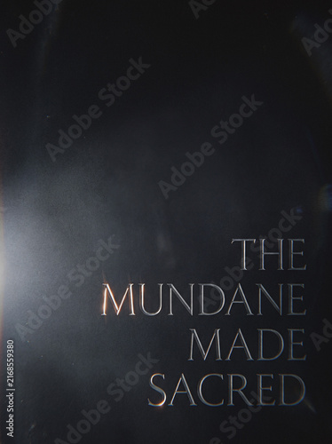 Dark moody background with elegant text overlay reading THE MUNDANE MADE SACRED, atmospheric quote design
