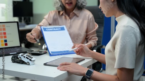 Car dealer agent shows color palette swatches and explains loan agreement contract to senior female buyer