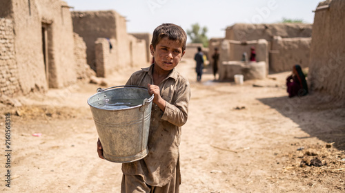 Young boy carrying a heavy water bucket in a rural village  