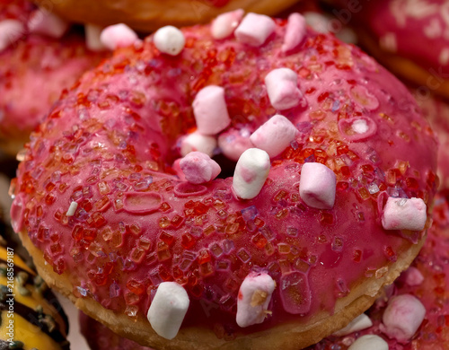 Fresh ring donuts covered with red glaze and white marshmallow pieces displayed in a bakery, showcasing sweet pastries arranged attractively for customers and shoppers
