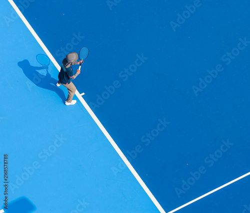 aerial view of a young male tennis player in action on a vibrant blue hard court. A sharp silhouette enhance this dynamic outdoor sports composition.
