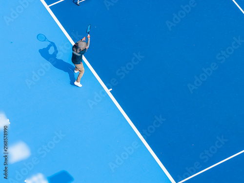 aerial view of a young male tennis player in action on a vibrant blue hard court. A sharp silhouette enhance this dynamic outdoor sports composition.