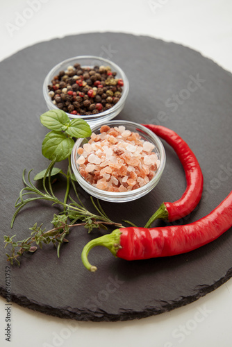 Fotografía Gourmet spices background closeup with organic seasoning ingredients, pink himalayan rock salt, peppercorn mix in bowls and red hot chili peppers on round black slate plate with left side copy space