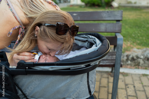 Fotografie Mother tenderly kissing baby in stroller outdoors