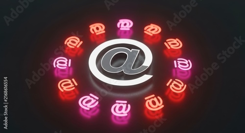 A large metallic at symbol is surrounded by a circular arrangement of smaller, glowing neon at signs on a dark, reflective surface.