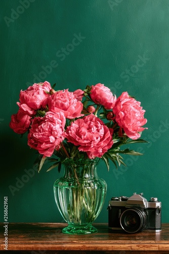 Vibrant pink peonies in a glass vase beside a vintage camera