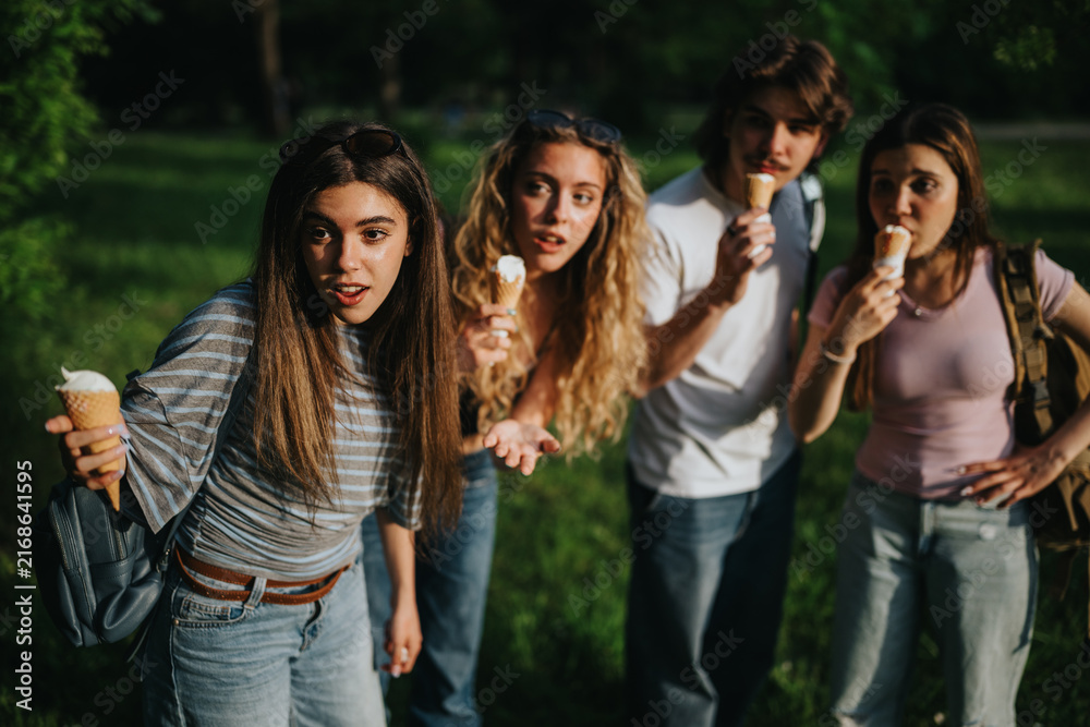 Fototapeta premium Teenagers eating ice cream cones together in a green park. A group of friends share a playful summer moment outdoors.