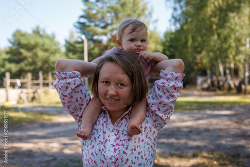 Woman carrying a baby on her shoulders outdoors on a sunny day
