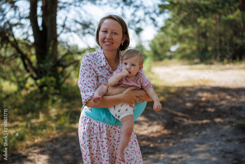 Woman holding a baby in a hipseat carrier on a forest path