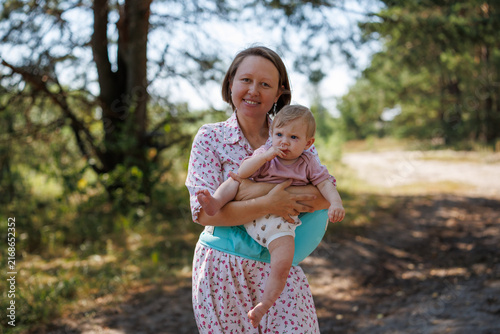 Woman holding a small baby in a hipseat carrier on a sandy forest path