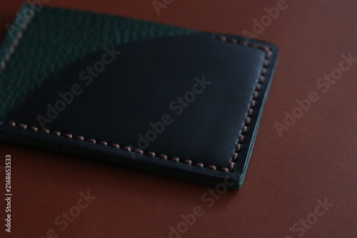Black leather card holder with belt strap detail on a dark background. Minimal fashion accessory photography showcasing compact design, craftsmanship, and modern everyday carry style.