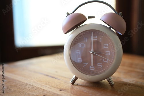 Bild auf Leinwand An alarm clock sits on a wooden table near a window, silhouetted against the light