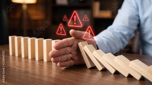 Businessman hand stopping falling wooden domino blocks for risk management and crisis prevention