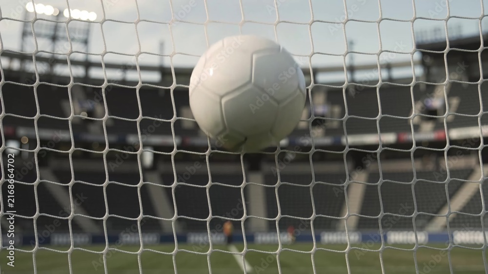Naklejka premium Soccer ball strikes the netting of a goal in a stadium, creating a splash effect as it impacts the mesh, showcasing the excitement of the game in action
