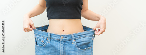 Foto Shape slender, thin waist, slim fit asian young woman, showing body shape her weight loss, happy wearing in big, large or oversize jeans, excess lose by diet and exercise
