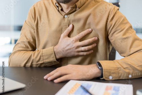 Fotografie Businessman sitting at a desk and suffering from sudden chest pain, placing a ha