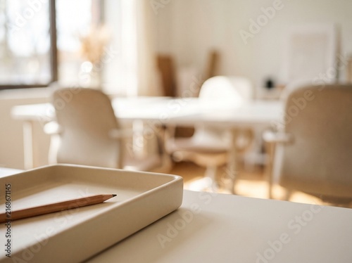 A close-up of a beige tray with a pencil on a desk, with a blurred modern office meeting room in the background.