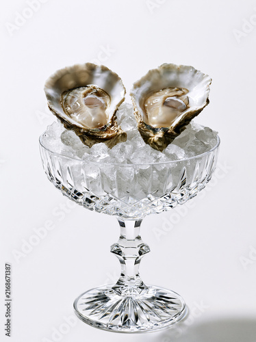 Deux huîtres fraîches posées sur un lit de glace pilée dans une élégante coupe en cristal, isolées sur fond blanc. Un visuel raffiné et luxueux idéal pour les cartes et menus de fête