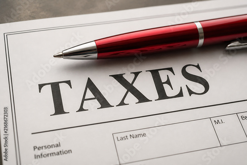 A red pen rests on a document titled TAXES, which has fields for personal information.