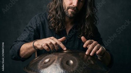Male musician with long hair plays metal handpan drum in a professional studio. Perfect for music therapy, relaxation articles, and meditation banners.