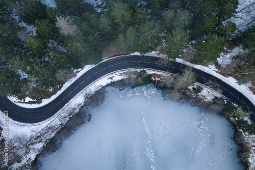 Aerial view of winding road beside a frozen lake in snowy winter forest
