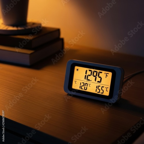 Illuminated Digital Thermometer Displaying Temperature and Time on a Wooden Surface with Warm Ambient Lighting