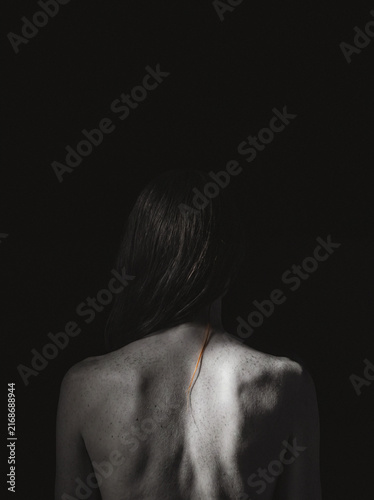 Woman's bare back and hair with faint necklace chain, moody dark portrait silhouette