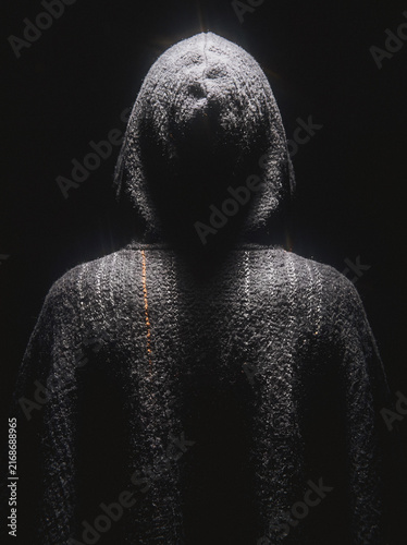 Hooded figure in knit sweater shrouded in shadow, mysterious dark portrait silhouette